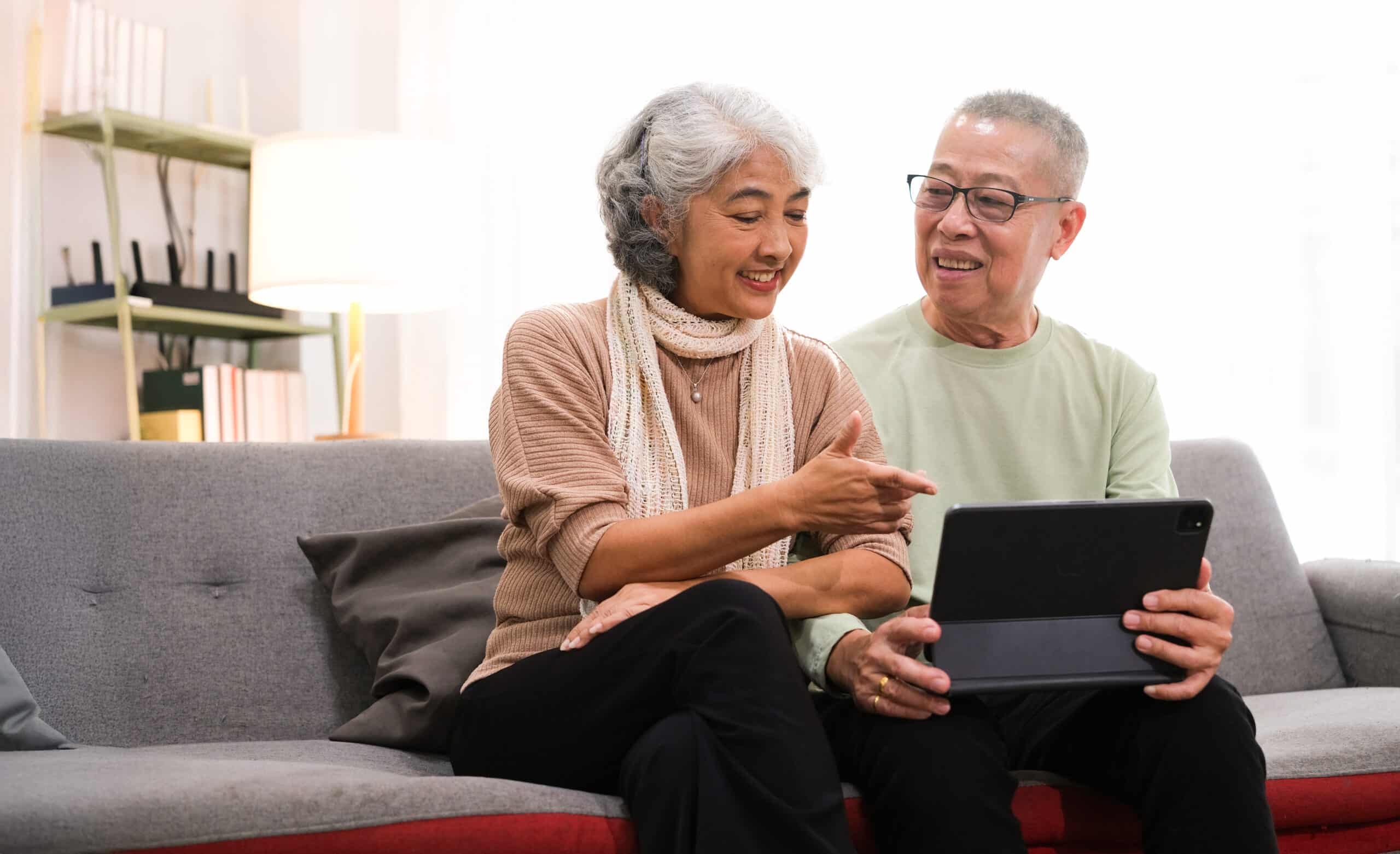 senior couple sitting on sofa using tablet while video call online with family in living room at home.